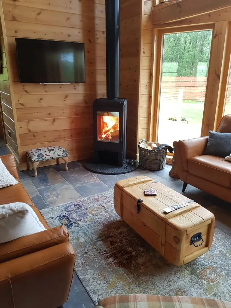 A cosy log stove in the living room of a log cabin with sofas and a coffee table