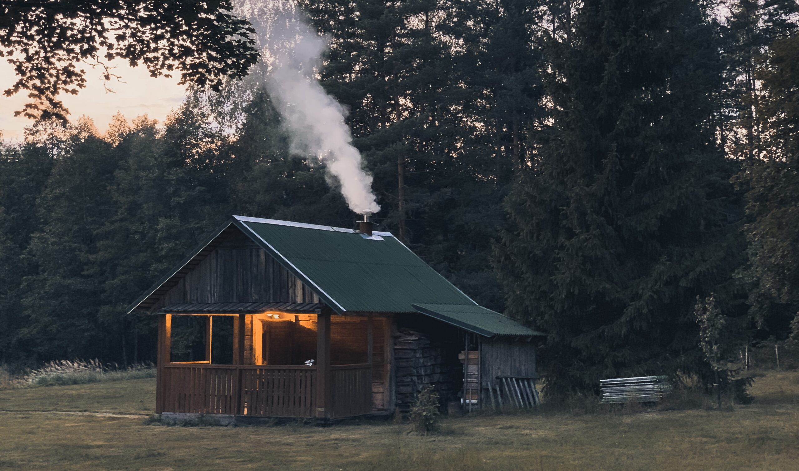 A rustic log cabin with smoke coming from the chimney and a light on the porch