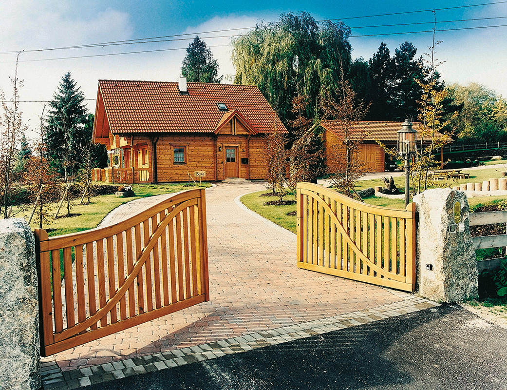 Photo showing the Koiteli chalet style log home with a long curved driveway and matching garage