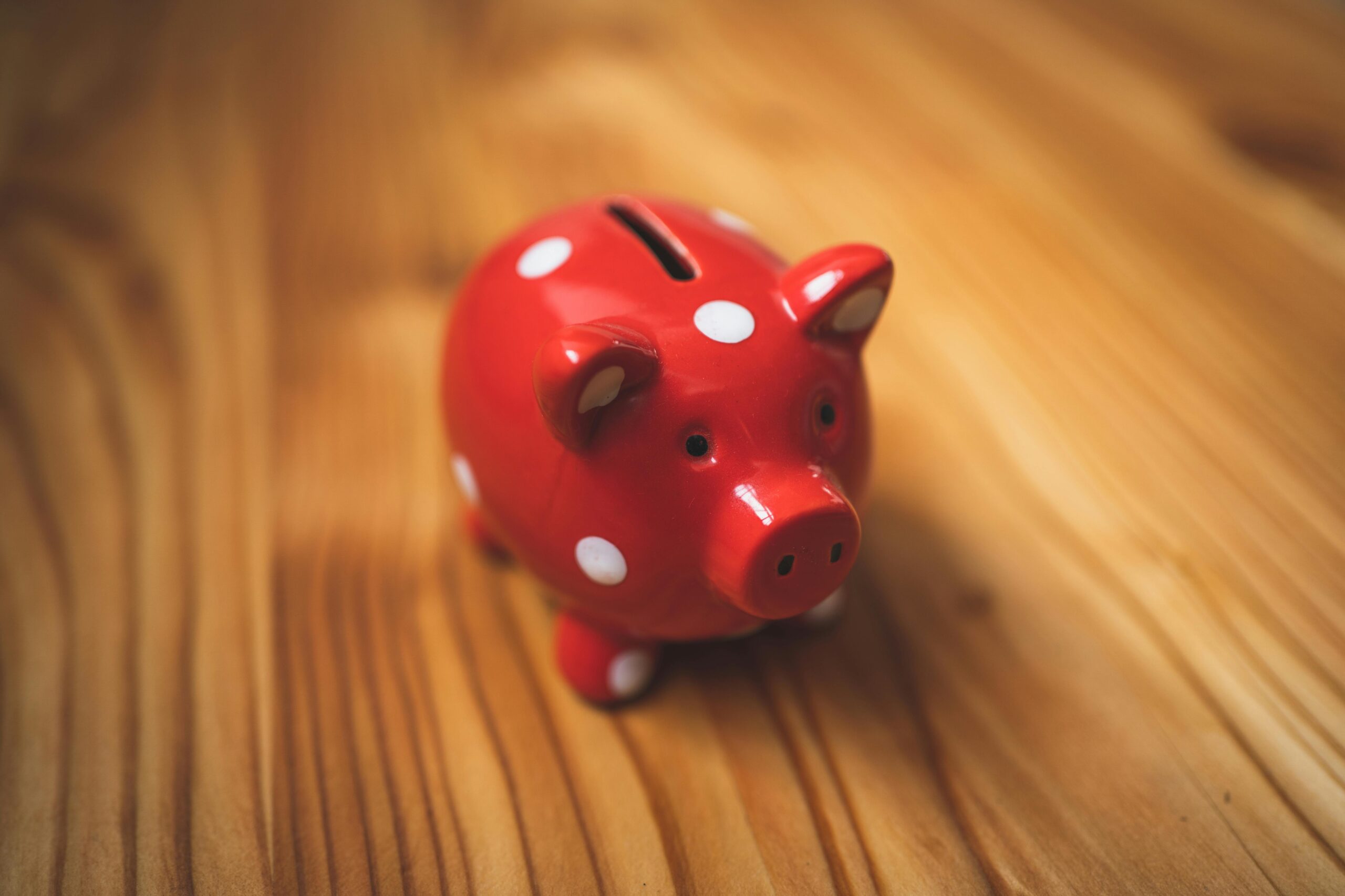 A photo of a red piggy bank with white spots on a wooden surface